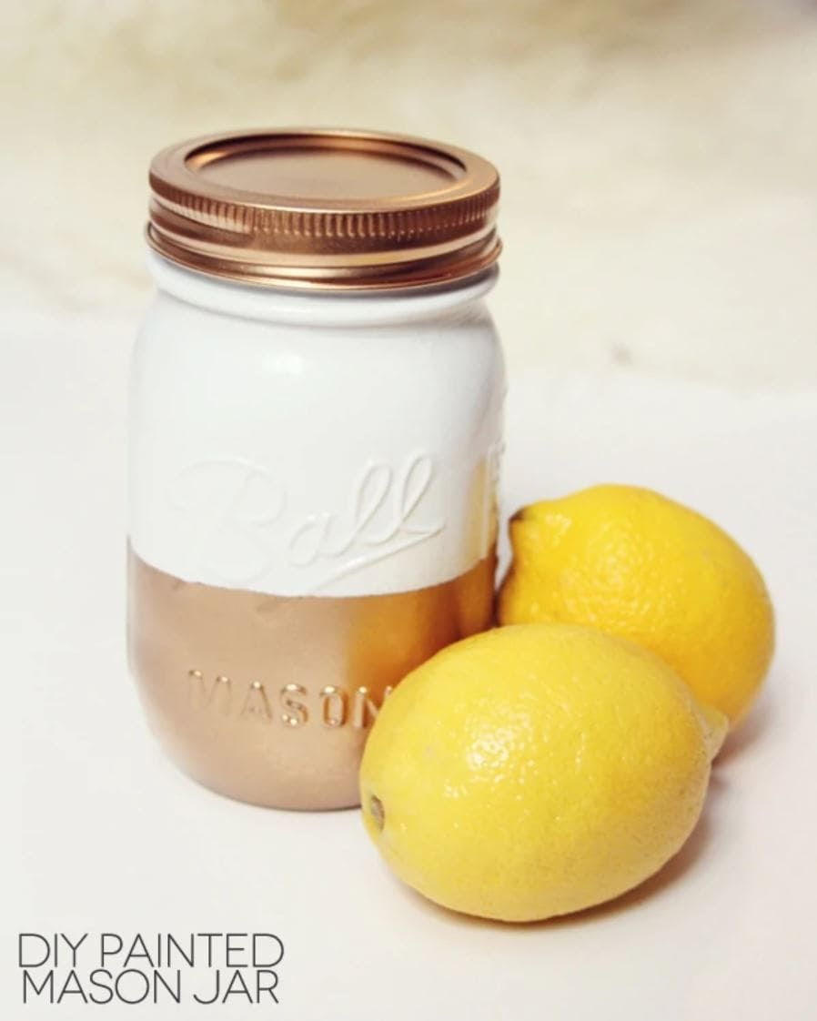 A mason jar painted with gold on the bottom and white on the top.