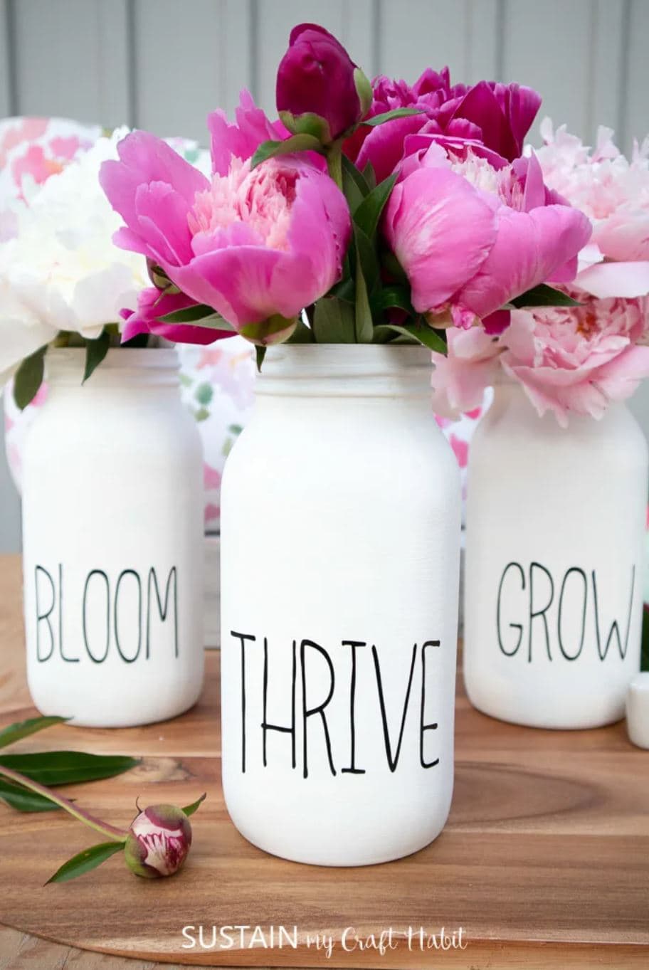 Three white painted mason jars with the words, "bloom", "thrive", and "grow" on them.