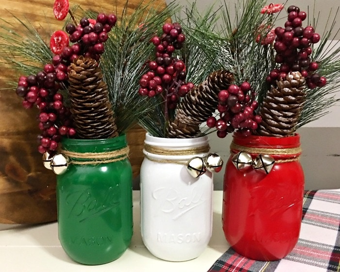 Three mason jars spray painted in green, white, and red with Christmas décor inside.