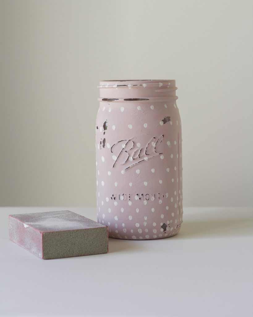 A quart mason jar painted with pink chalk paint and white polka dots distressed with a sanding block.