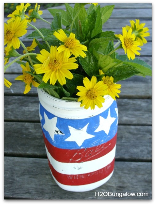 A stars and stripes mason jar with yellow flowers inside.