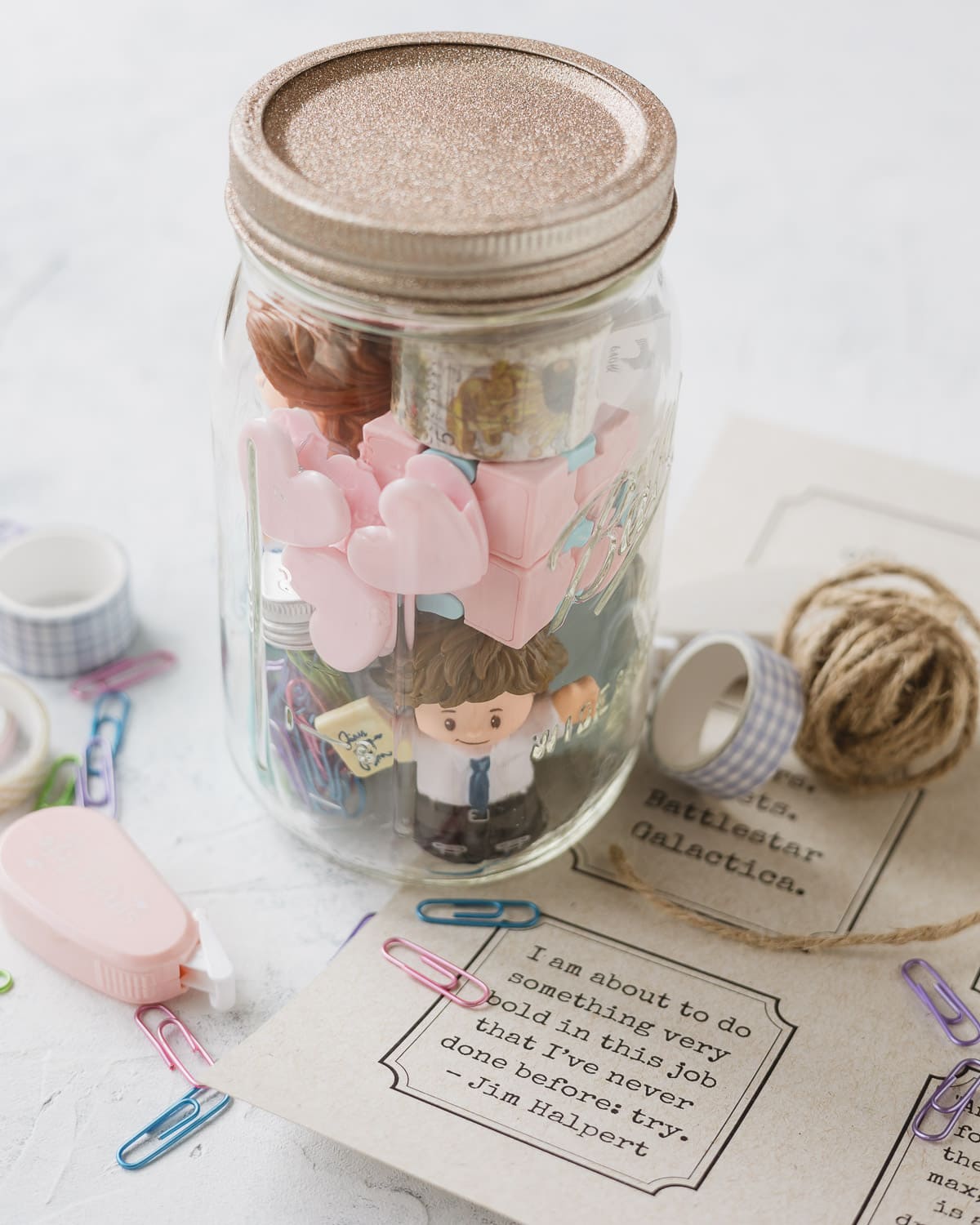 Gift tags, twine, washi tape, corrector tape, and other office supplies packed into a mason jar with a glittery lid.