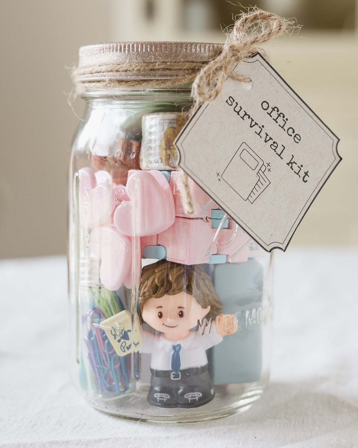 A mason jar filled with office supplies, a "Jim" figurine from The Office and a tag that reads, "Office Survival Kit".