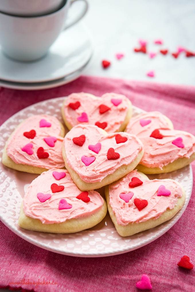 Pink frosted sugar cookies decorated with heart sprinkles and arranged on a pink plate.