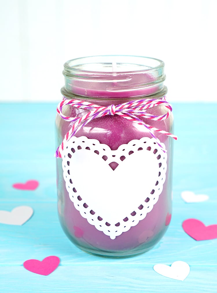 A pink mason jar candle with a heart cutout on the jar.