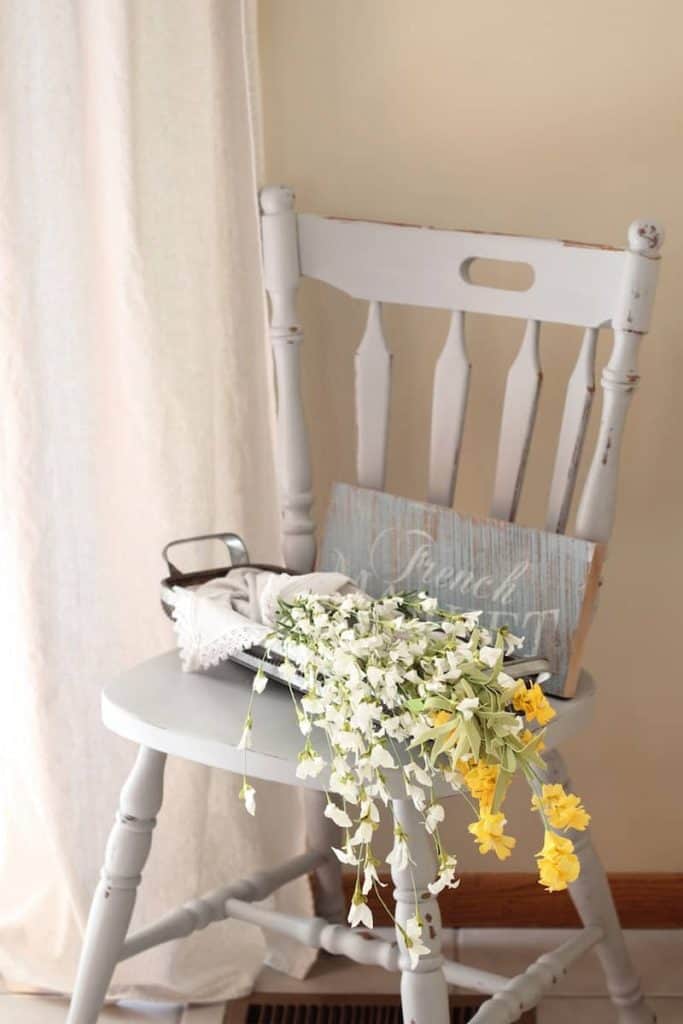 A farmhouse chair painted gray with a basket of faux flowers on top. 