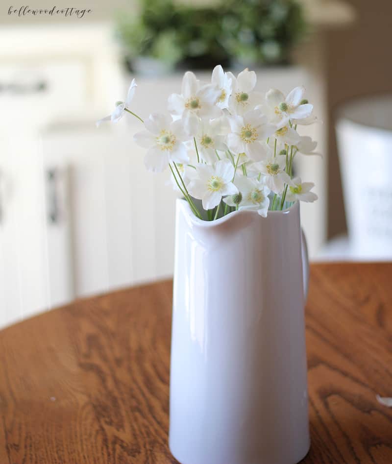 A white pitcher with flowers inside.