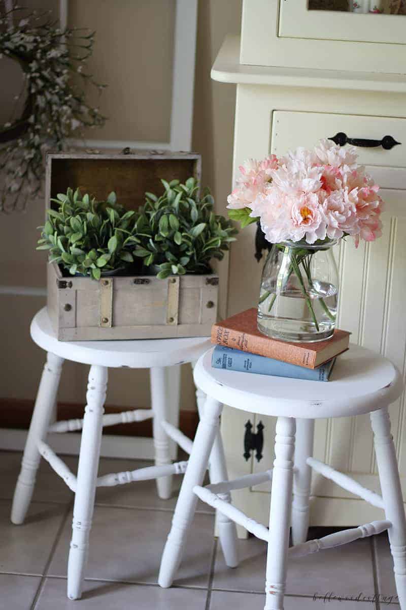 Farmhouse stools painted white and distressed with decorative greenery on top.