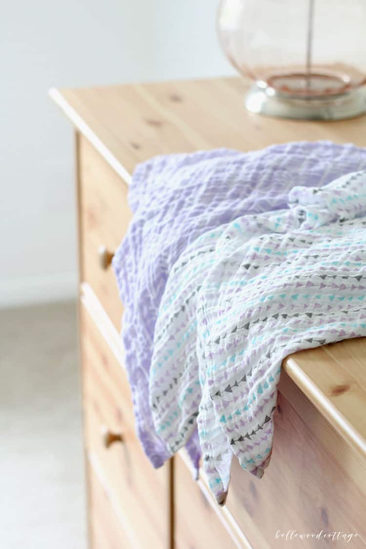 Two swaddle blankets on a pine dresser.