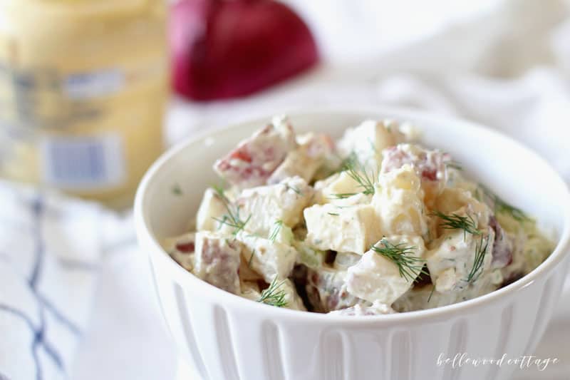 A white bowl filled with potato salad and garnished with dill.