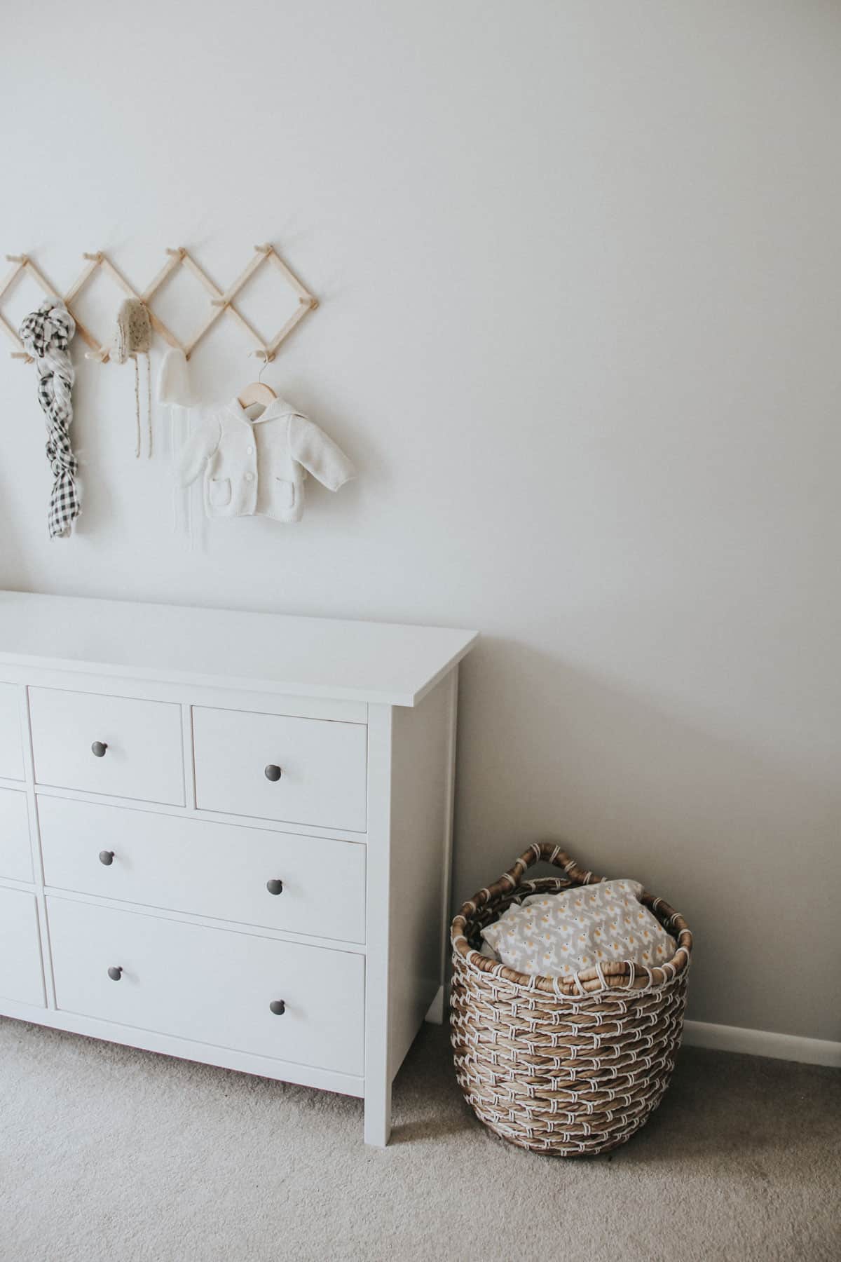 Large basket filled with baby blankets alongside a white Ikea dresser in a neutral baby room.