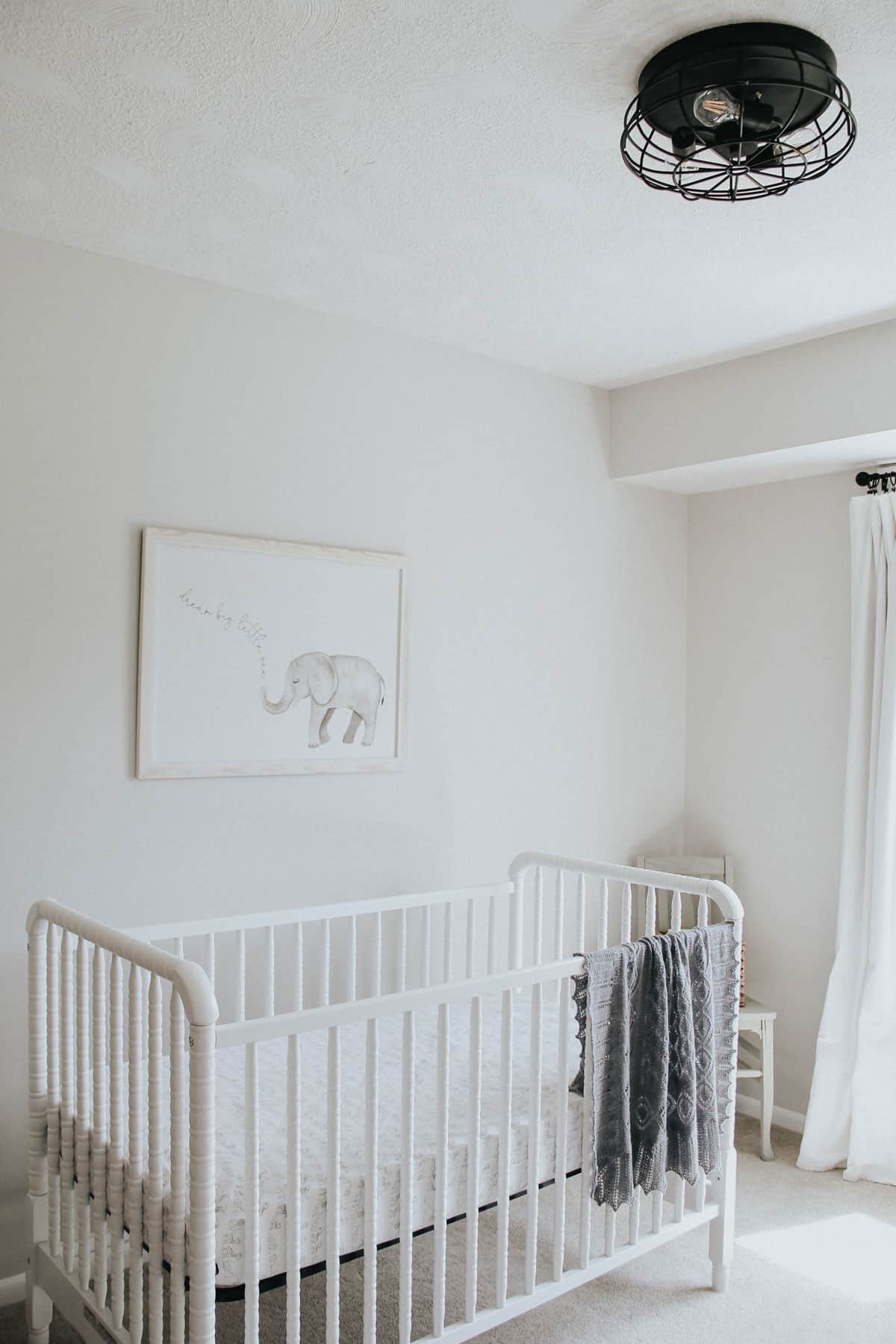 Jenny Lind crib with knitted blanket in a neutral nursery with a farmhouse light.