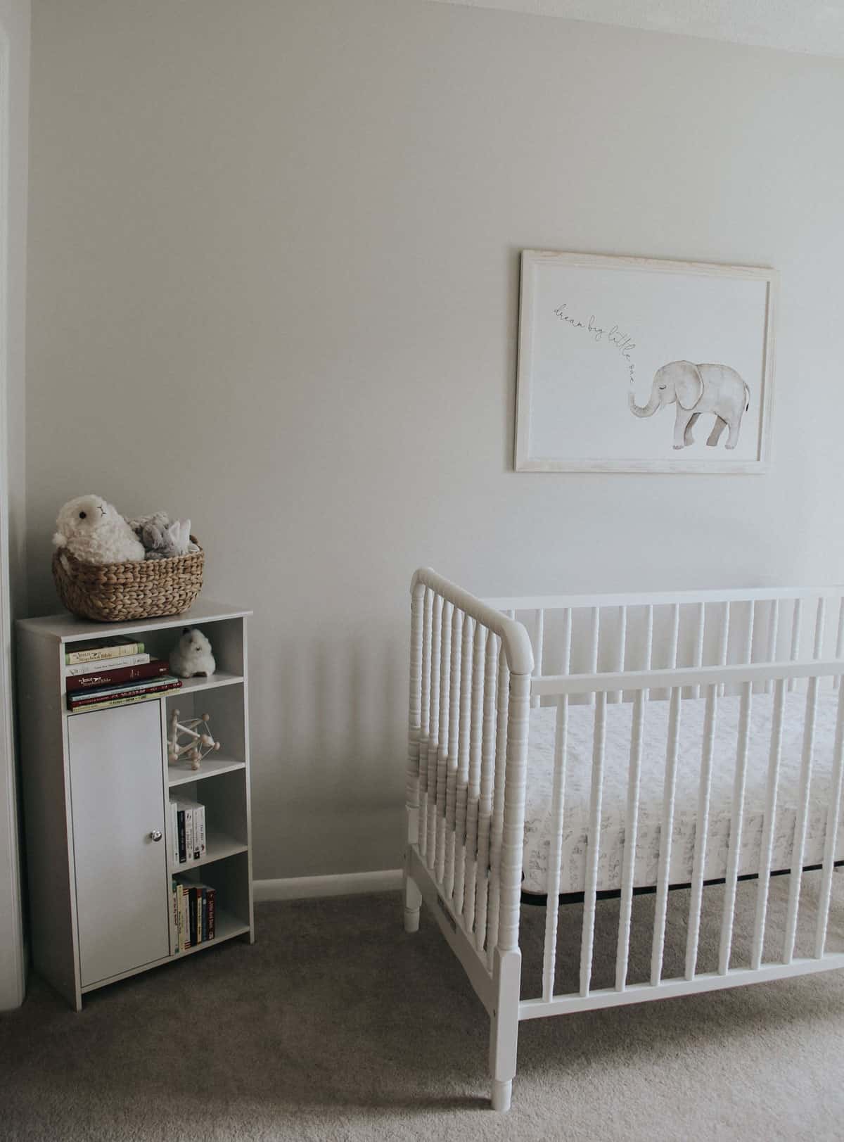 Baby bookshelf, stuffed animals and a white Jenny Lind crib in a nursery.