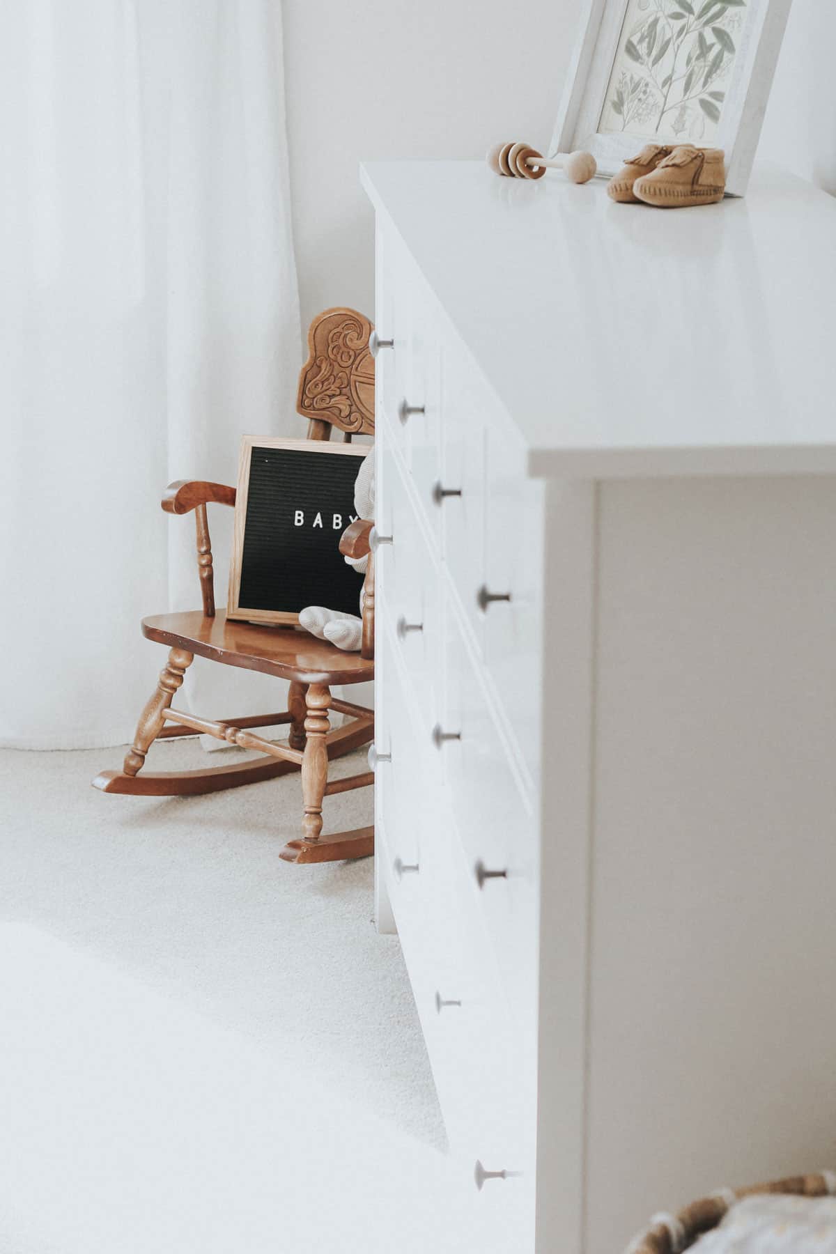 Rocking chair, letter board, and white dresser in a neutral nursery.