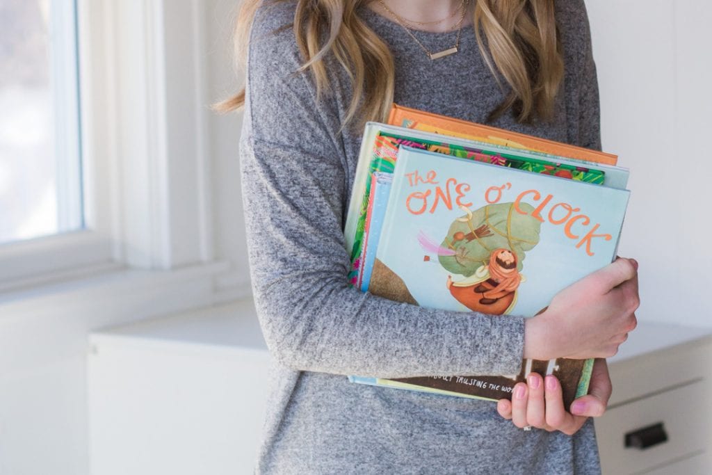 Holding a stack of picture books—part of the best picture book booklist for kids.