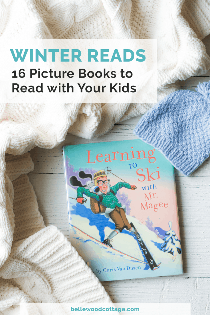 A winter picture book on a wooden surface surrounded by a winter hat and cozy blanket.