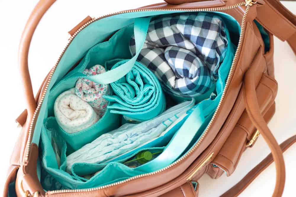 An interior view of a Lily Jade diaper bag packed with a baby wrap, extra clothing, and diapers.