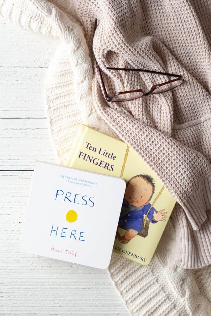 Two board books (Press Here and Ten Little Fingers, Ten Little Toes) on a wooden surface.