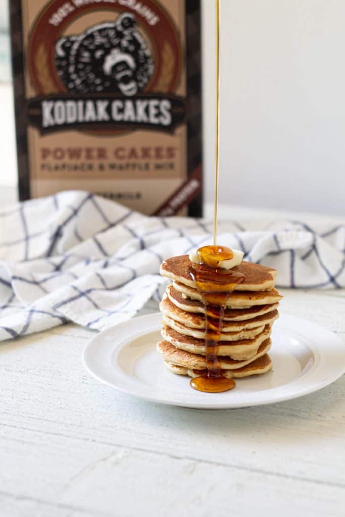 Stack of pancakes with butter on top and syrup being poured over.