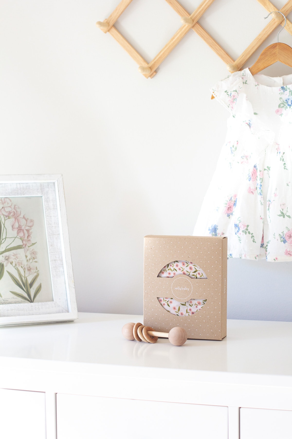 A Solly Baby Wrap on a white dresser with an heirloom wooden rattle in front of it.