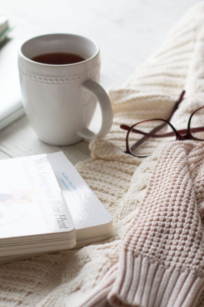 A mug of tea, glasses, books, and a fall sweater.