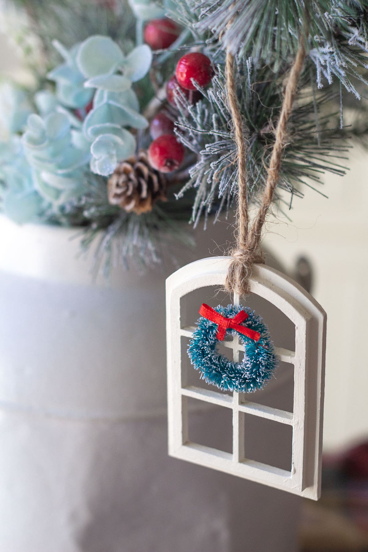 A handmade Christmas window ornament hanging from a decorative pine bough.