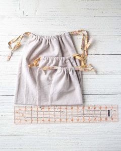 Three drawstring bags on a wooden surface with a ruler.