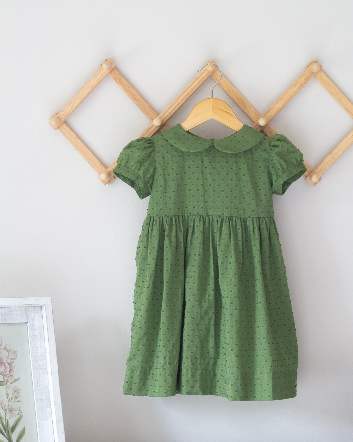 A green toddler dress with a peter pan collar hanging on a wooden hanger.