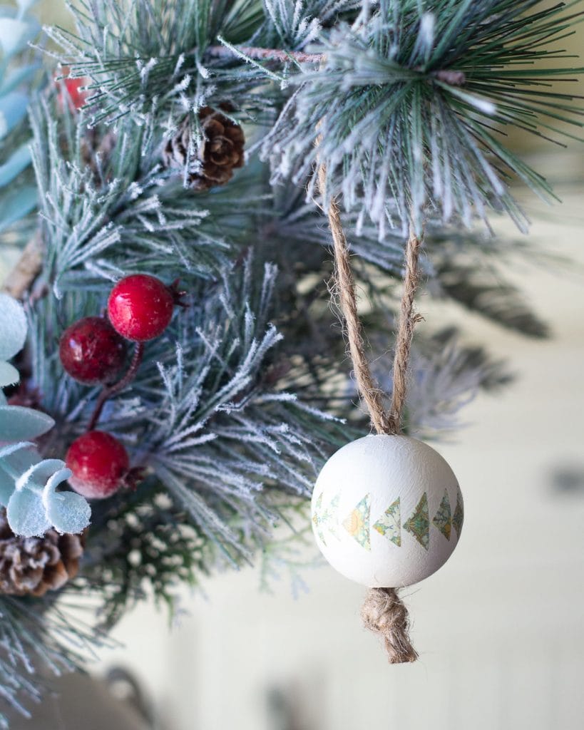 A painted Christmas tree ornament decorated with washi tape hanging on a faux pine bough.