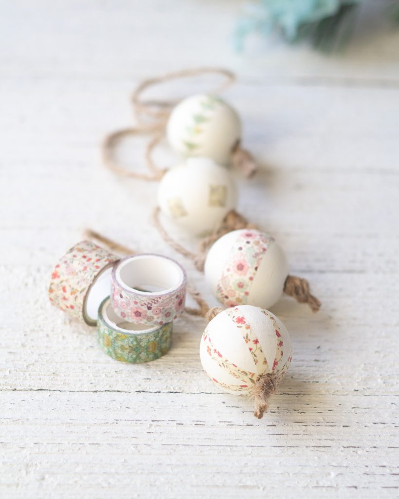 Spools of washi tape and decorated Christmas ornaments on a wooden surface.