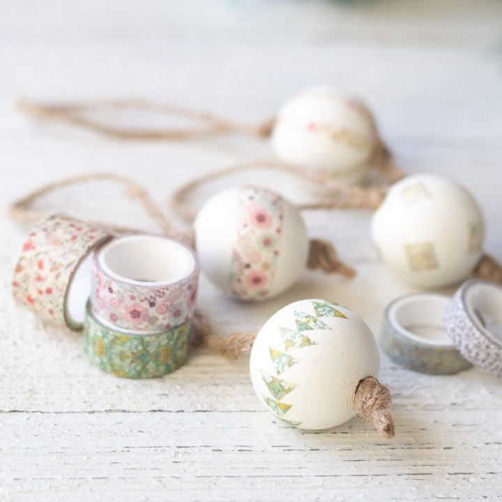 Spools of washi tape and decorated Christmas ornaments on a wooden surface.