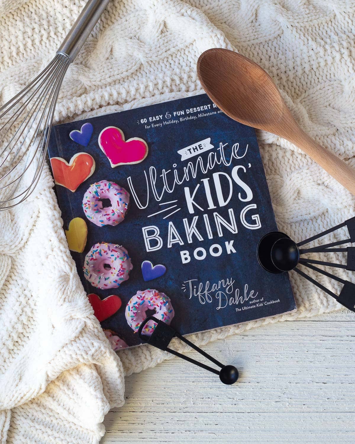 A baking book for kids surrounded by teaspoons and a wooden spoon.