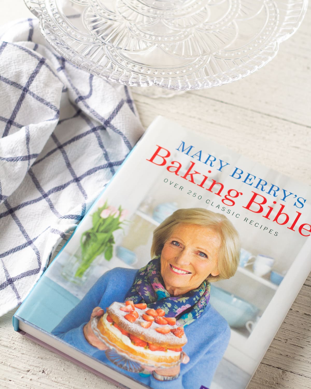 Mary Berry's Baking Bible, a cake stand, and an IKEA towel on a wooden surface.