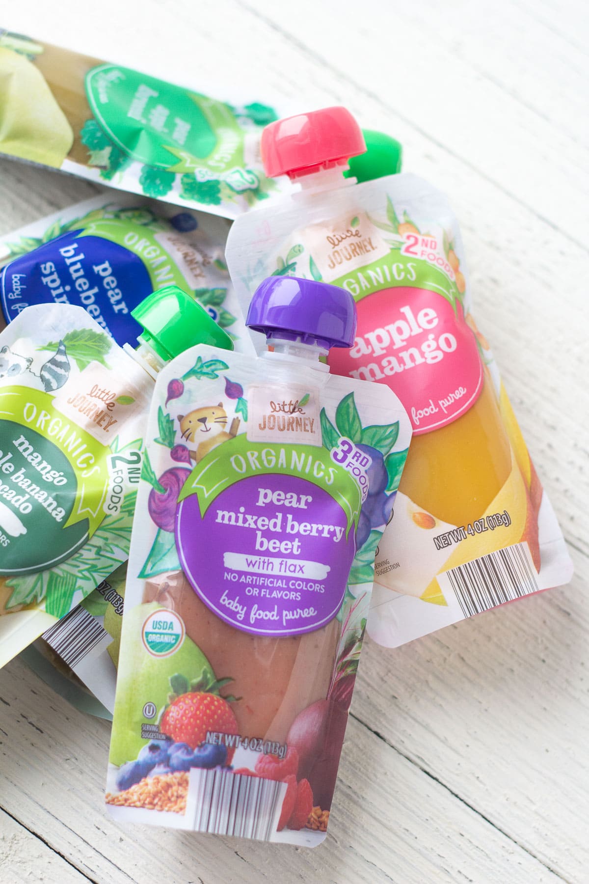 A selection of Little Journey Baby Food Pouches on a wooden surface.