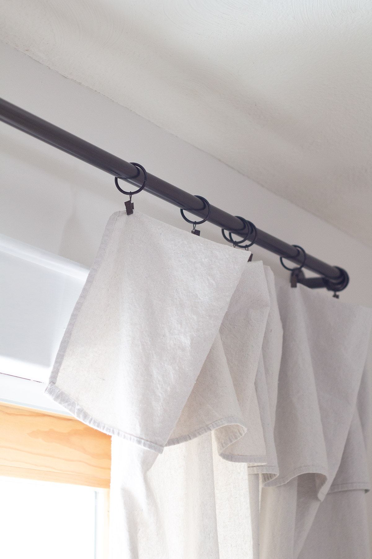 A curtain hanging on a black curtain rod with clips.