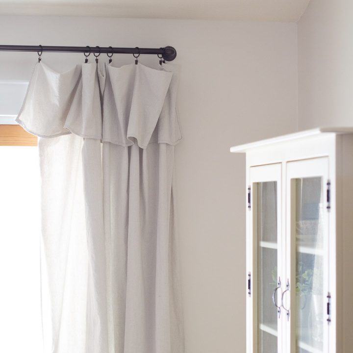 A cream-colored hutch and drop cloth curtains in a farmhouse-style dining room.