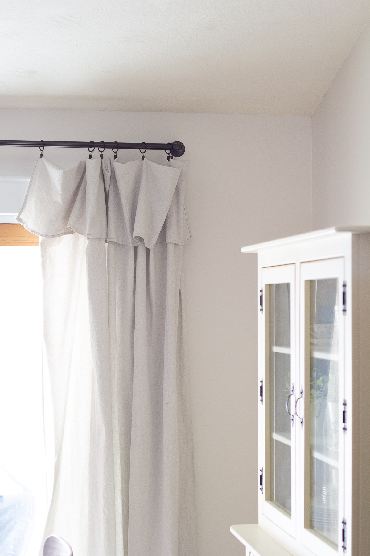 A cream-colored hutch and drop cloth curtains in a farmhouse-style dining room.