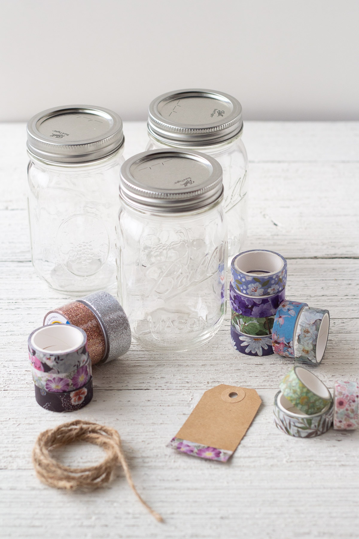 Mason jars, washi tape, twine, and a gift tag on a wooden surface.