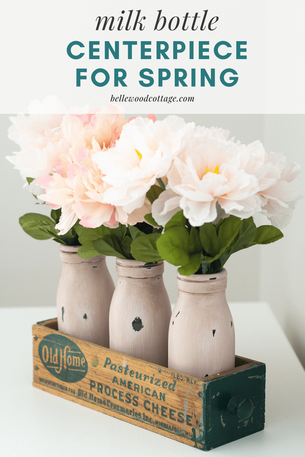 Painted milk bottles in a vintage cheese box with the words, "Milk Bottle Centerpiece for Spring"