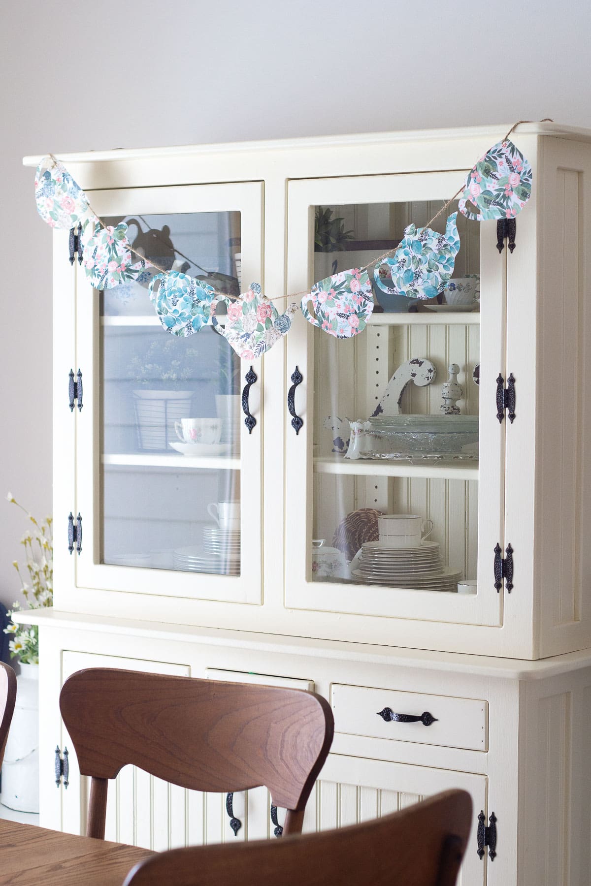 A teapot garland made from scrapbook paper hanging on farmhouse hutch.