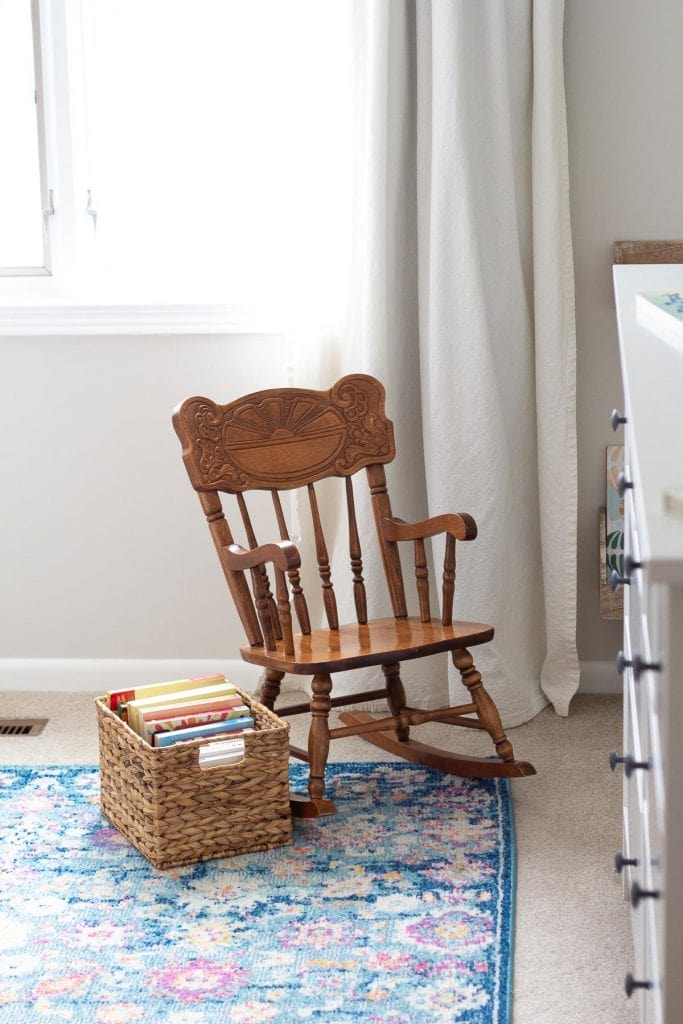 Baby board books stored in a basket alongside a vintage toddler's rocking chair.
