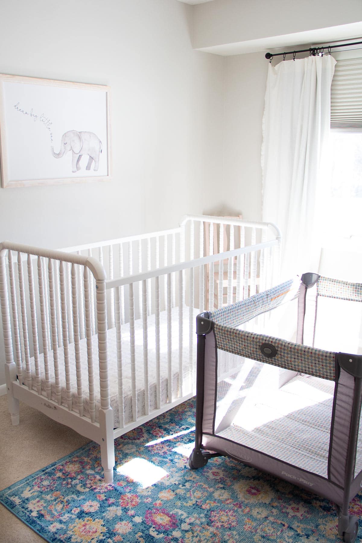 A white Jenny Lind Crib alongside a gray Graco pack and play.