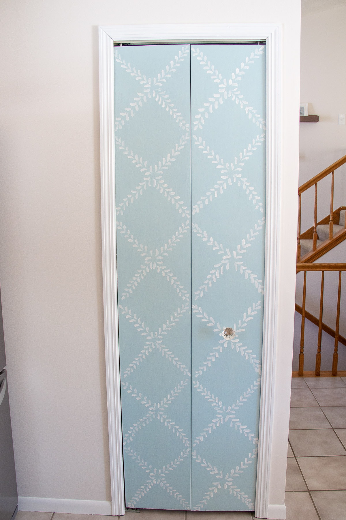 A bi-fold pantry door painted with light blue chalk paint and a floral design.