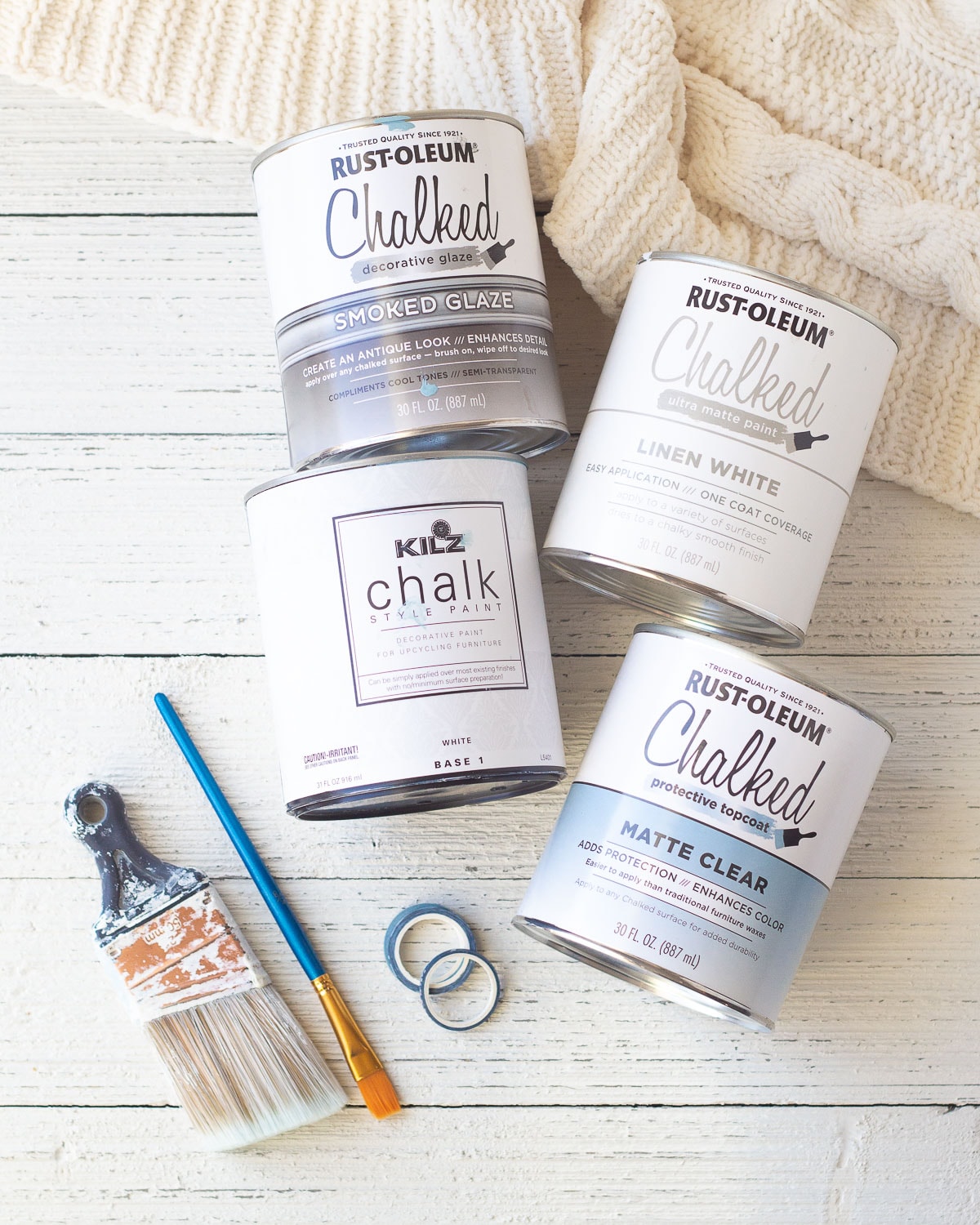 Chalk paint cans, paintbrushes, and washi tape on a wooden surface.