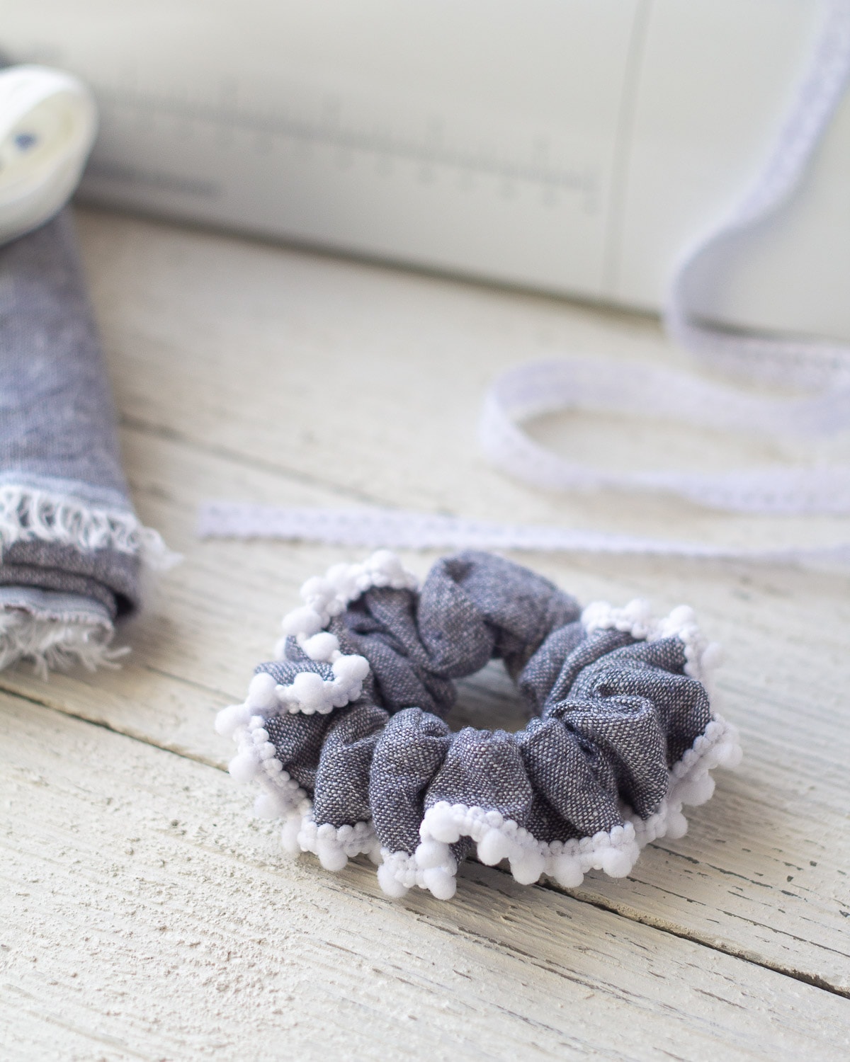 Scrunchie sewn with linen and edged with a white pom-pom trim.