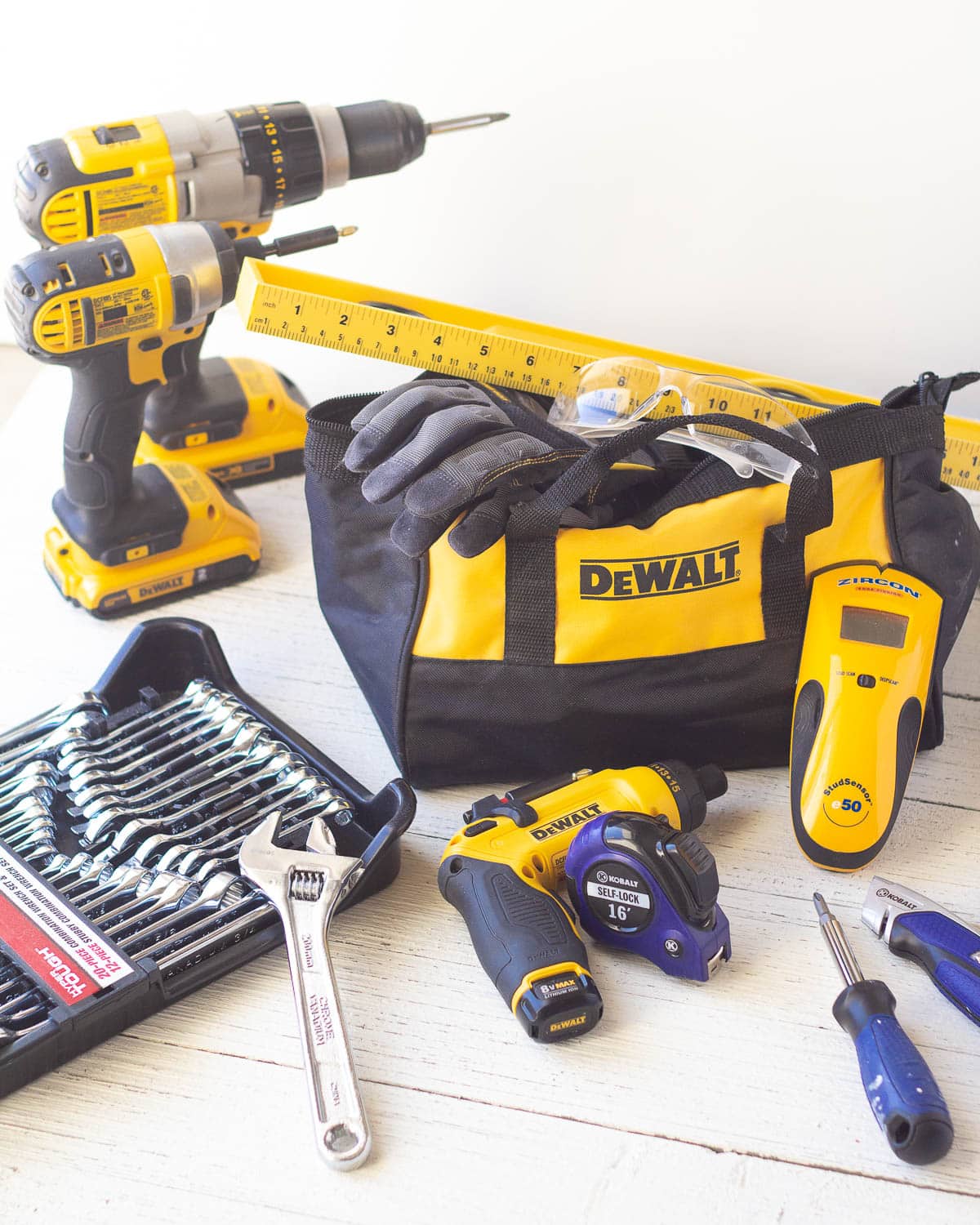 A tool bag surrounded by a stud finder, tape measure, drills, and other similar tools.