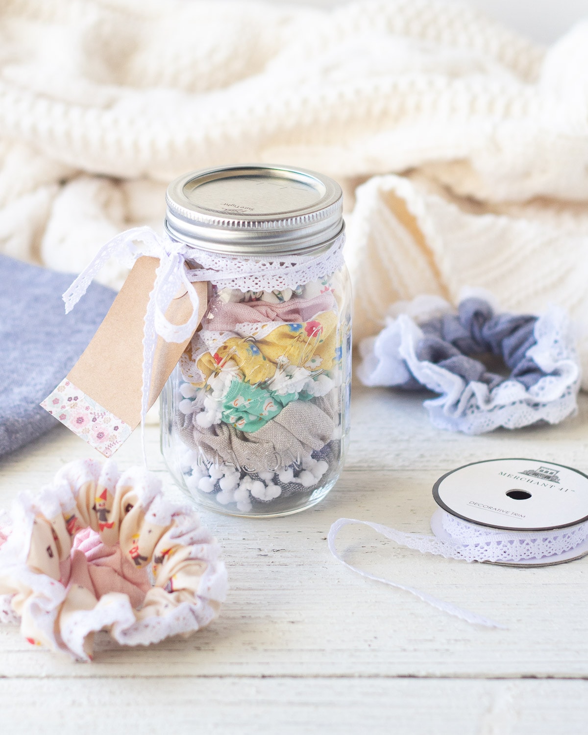 A mason filled with handmade scrunchies and surrounded by more scrunchies, fabric, and lace trim.