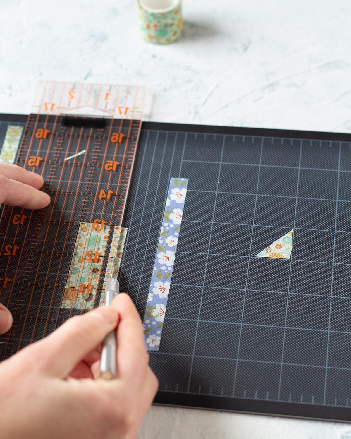 Using a cutting mat, ruler, and a craft knife to cut washi tape into thin strips.