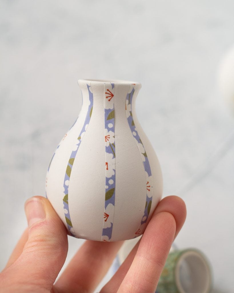A white bud vase with floral washi tape decorating it.