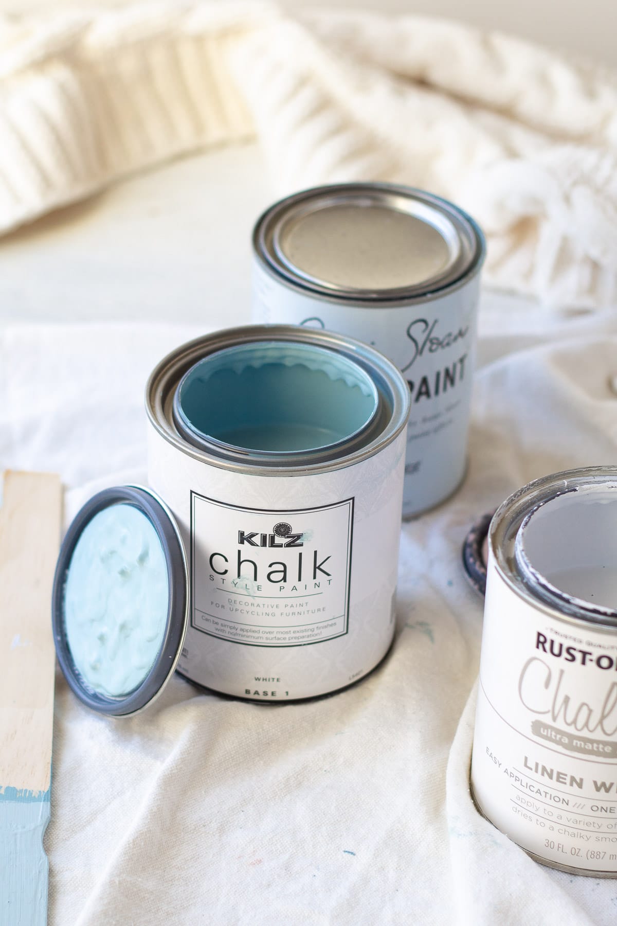 An open quart of KILZ Chalk Style Paint in Blue Juniper on a canvas drop cloth.